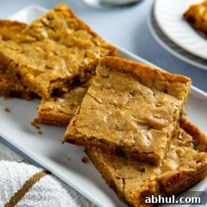 Several baked and sliced blondies stacked on a white rectangular platter.