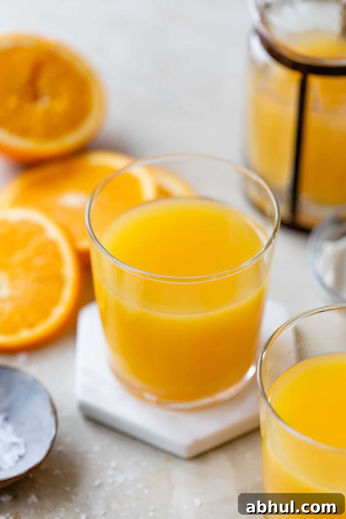 orange juice in a glass surrounded by sliced oranges and a small dish of sea salt