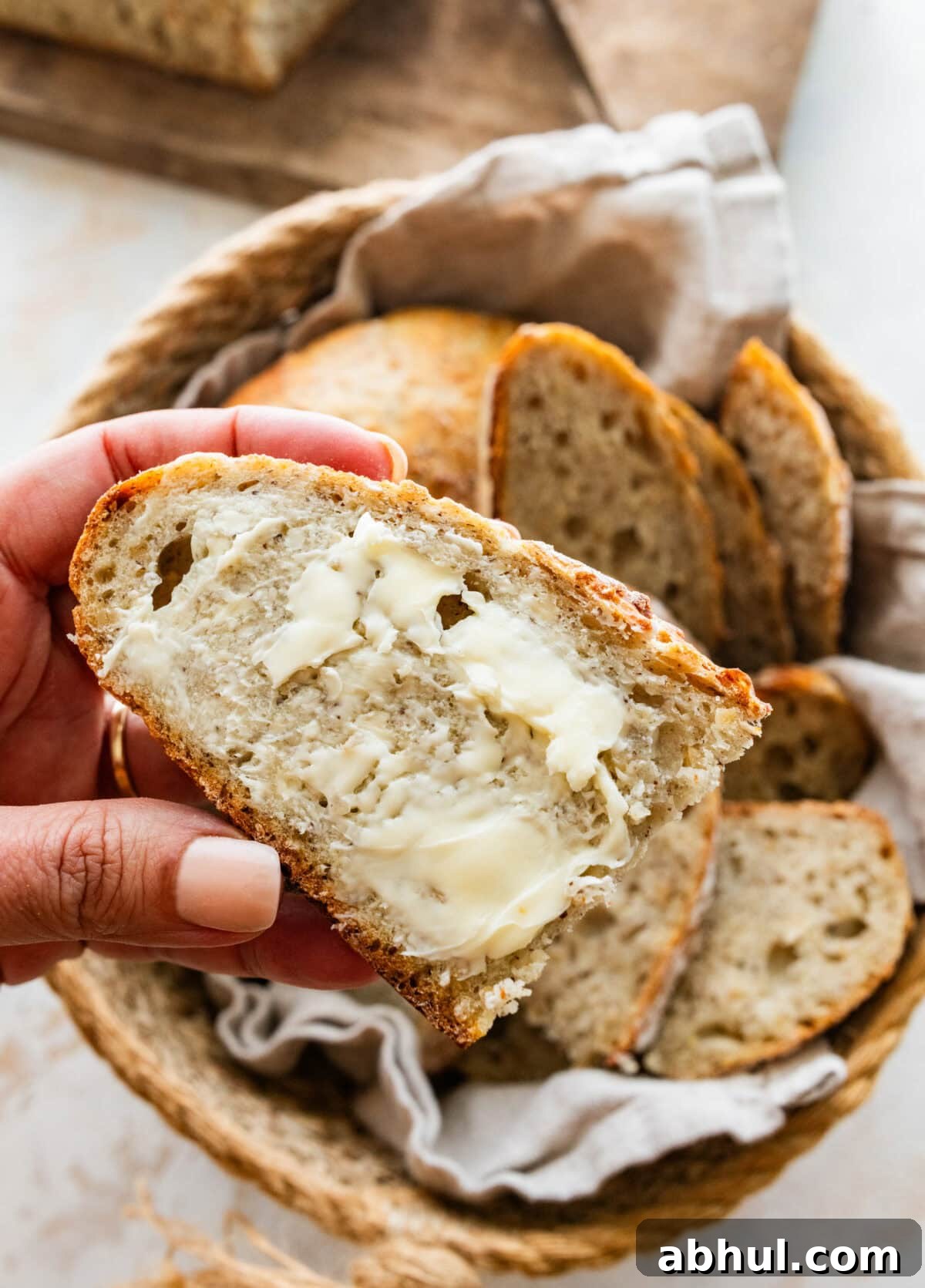 A hand holding up a slice of crusty Italian bread spread with butter. 