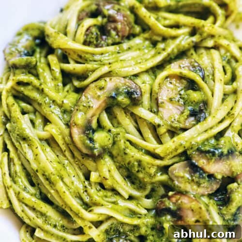 closeup of linguine pasta in pesto sauce with chopped mushrooms.