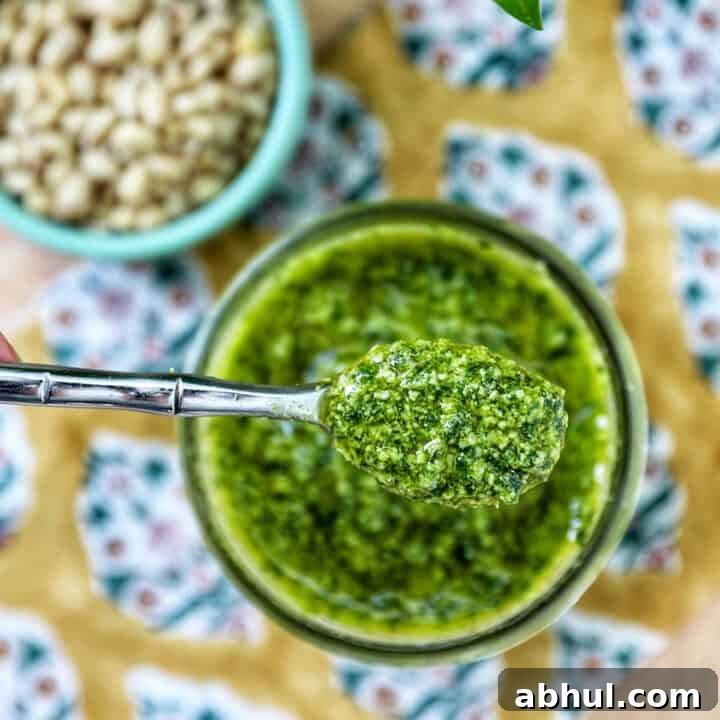 fresh basil pesto in a jar being spooned out of the jar.