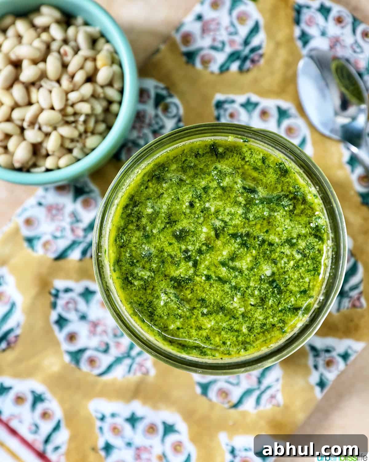 pesto in a mason jar next to a bowl of pine nuts and basil leaves.