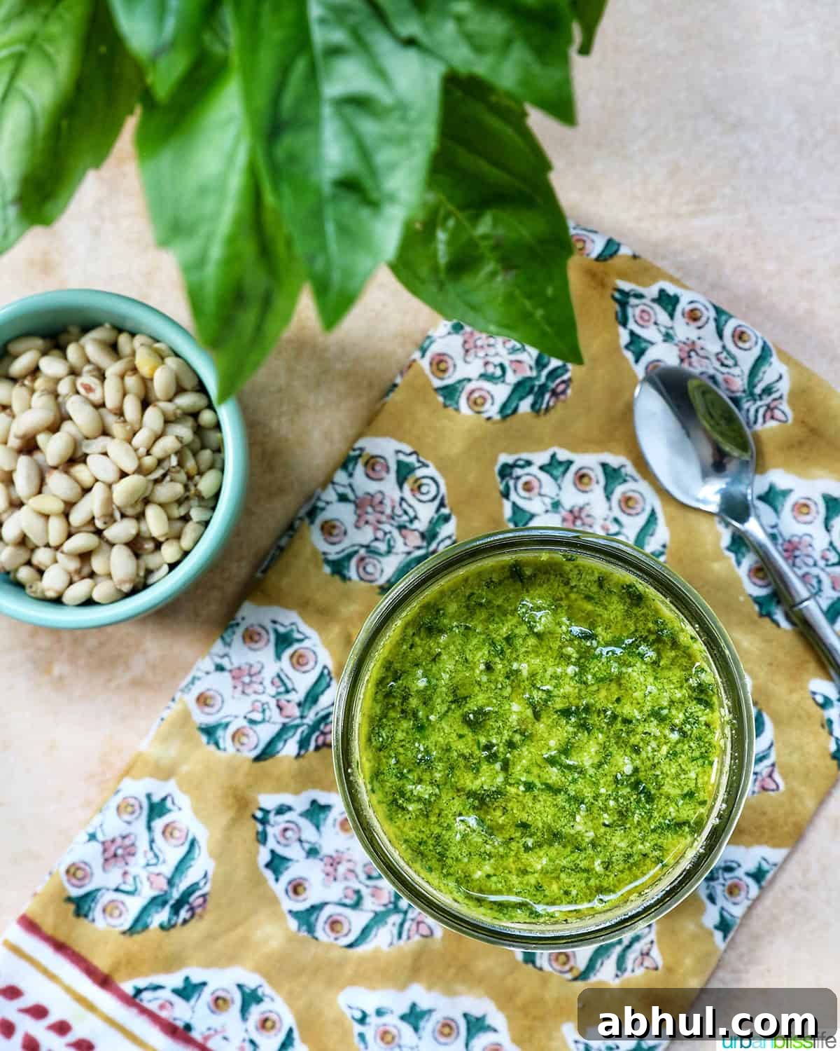 pesto in a mason jar next to a bowl of pine nuts and basil leaves.