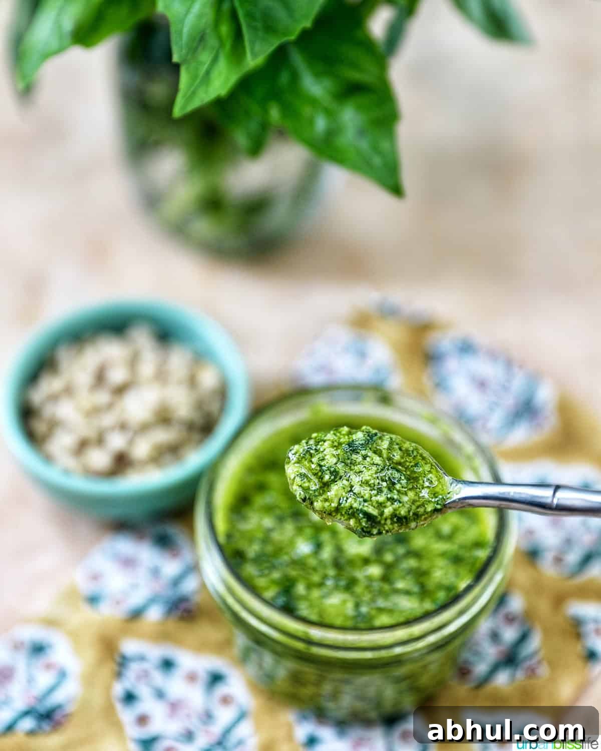 mason jar with spoon full of basil pesto next to a bowl of pine nuts.