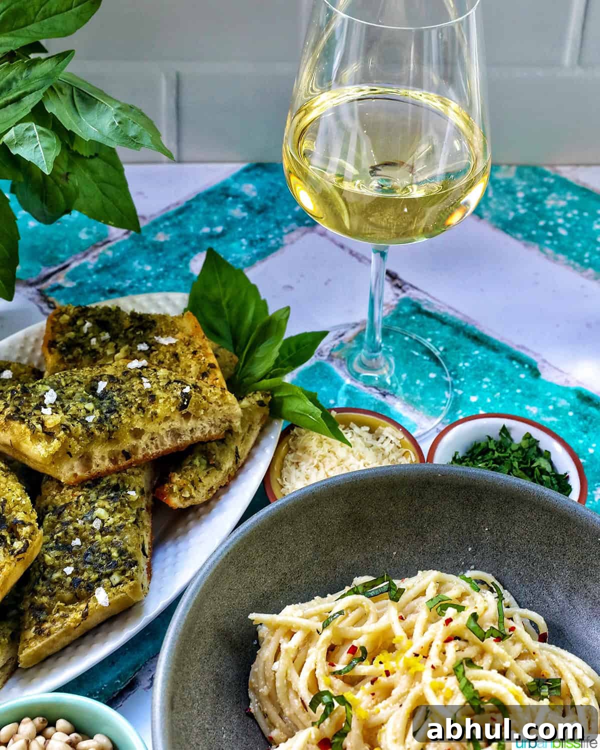 glass of wine next to plates of pesto bread and tahini pasta.