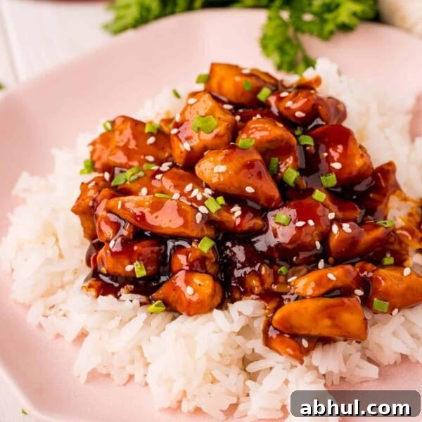 Bourbon chicken served on rice with sesame seeds and green onions.