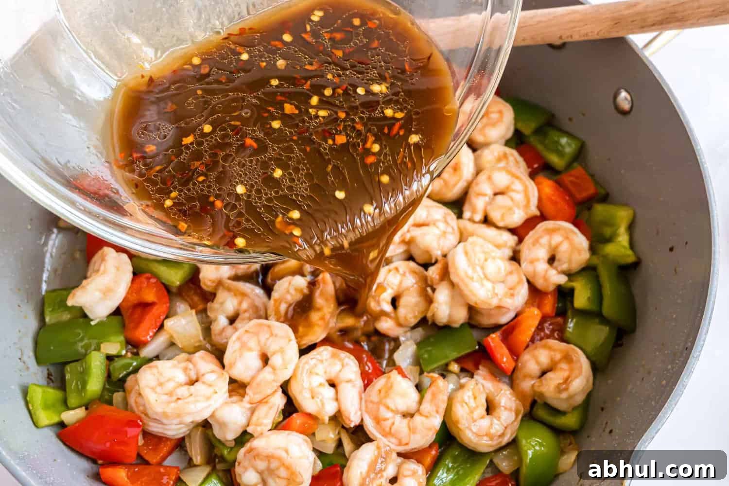 Sauce being added to cooked shrimp and vegetables.