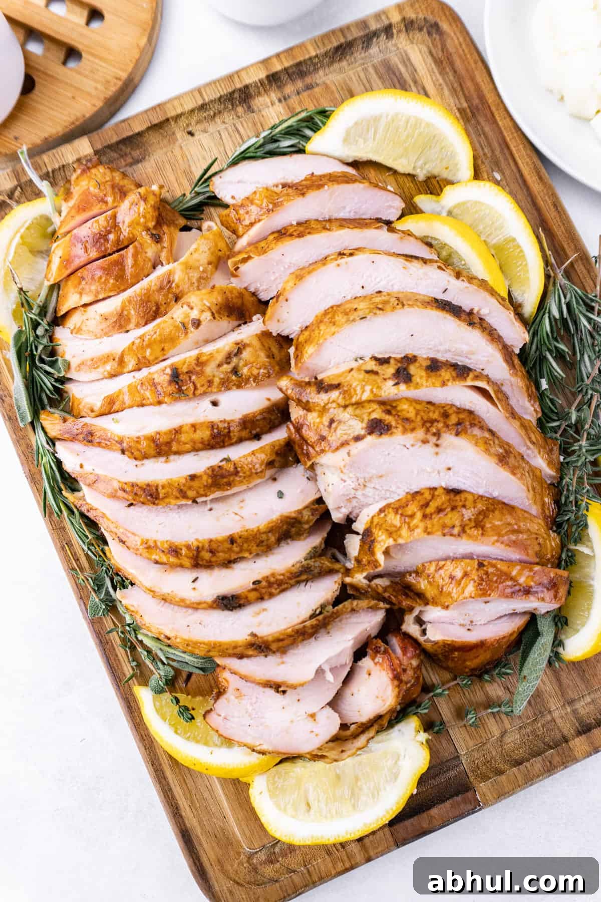 Sliced smoked turkey breast on a wooden cutting board surrounded by lemon slices and fresh rosemary.