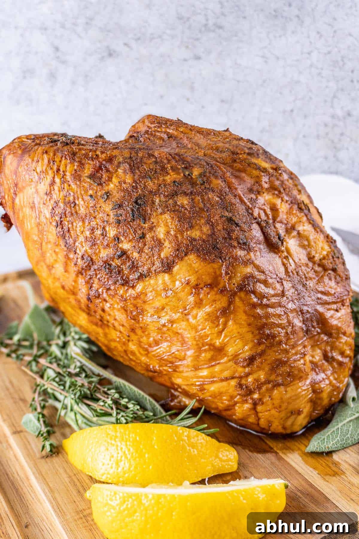 Whole smoked turkey breast on a wooden cutting board surrounded by lemon slices and fresh rosemary.