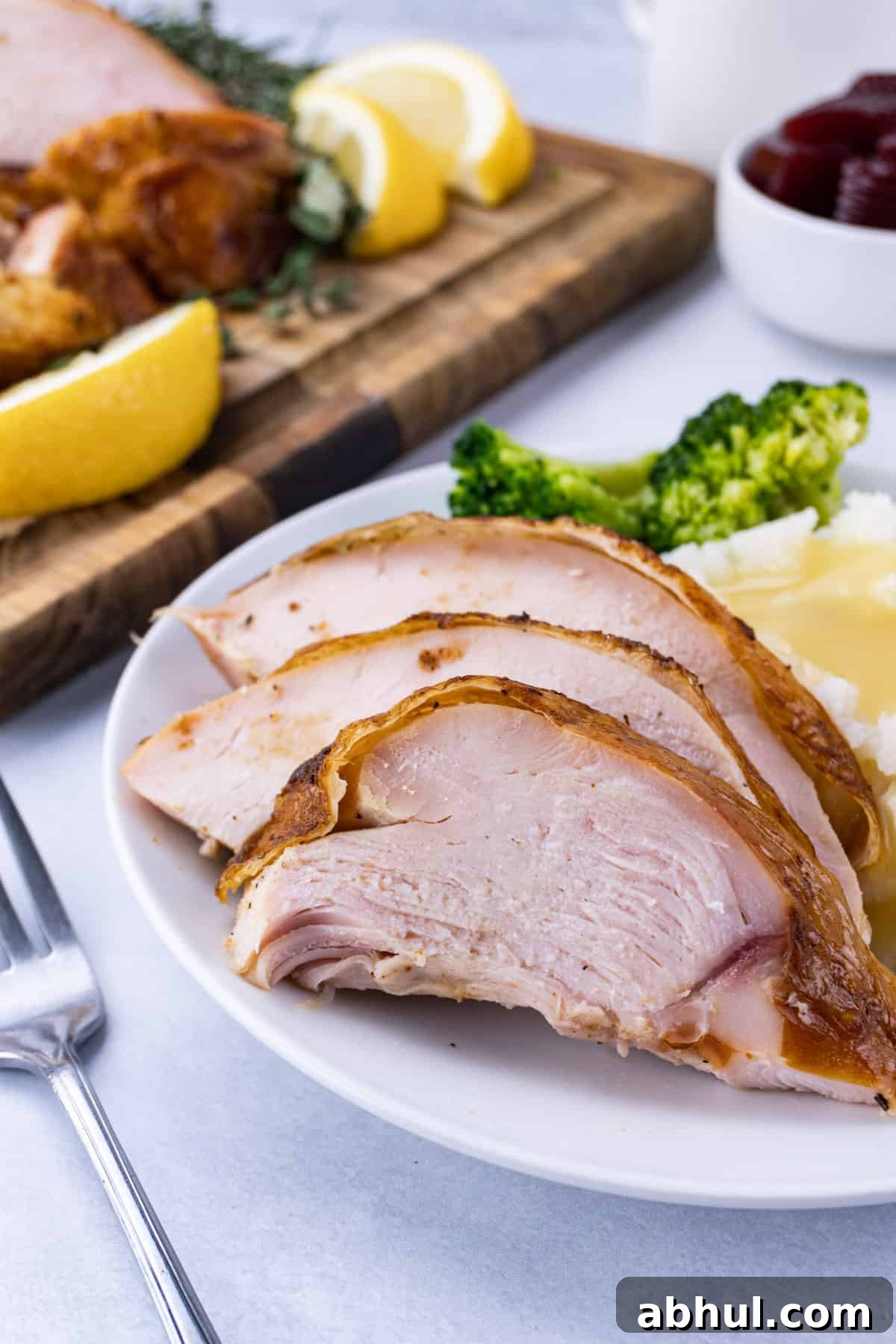Sliced smoked turkey breast on a plate next to broccoli and mashed potatoes.