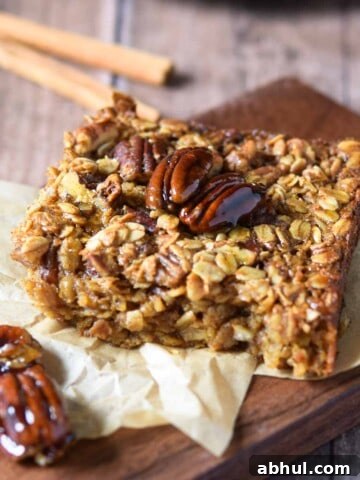 Baked pecan pie oatmeal on a wood slab with cinnamon sticks in the background.
