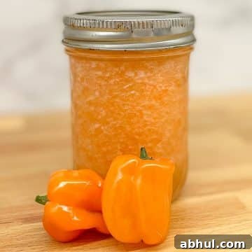 Pineapple habanero sauce in a glass jar with two habaneros on a butcher block counter.