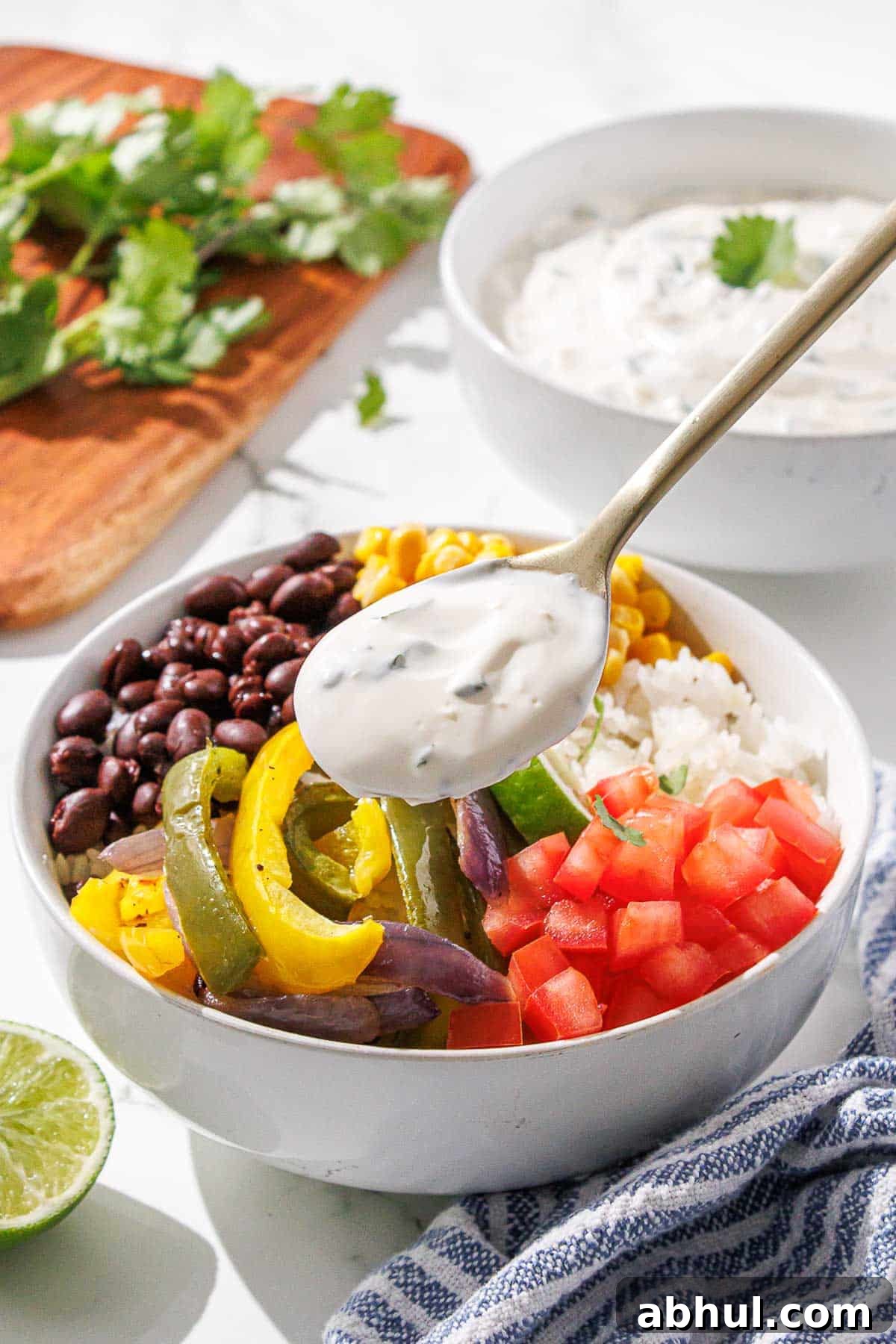 A colorful burrito bowl with a dollop of cilantro lime crema being added from a spoon.