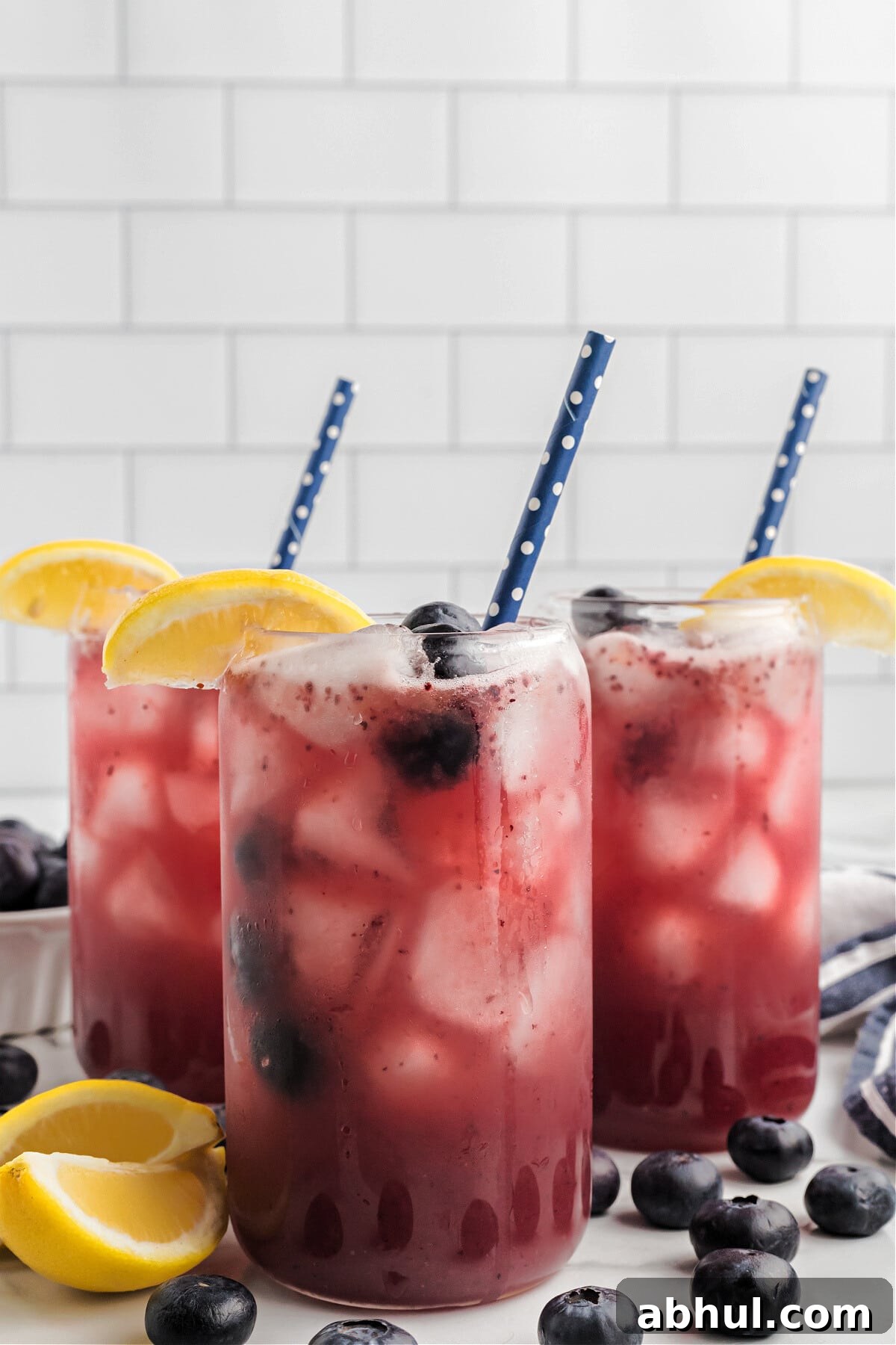 Refreshing Blueberry Lemonade Recipe with Fresh Citrus Twist 2 blueberry lemonade in glasses with blue straws, fresh lemon slice and blueberries