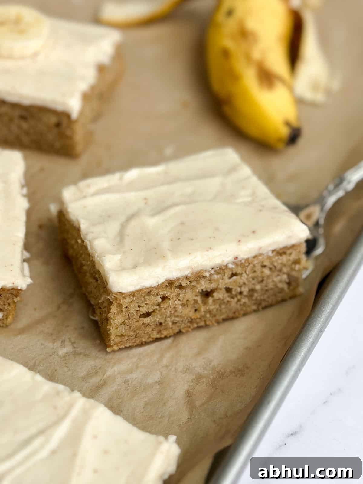 a close up of a single slice of the brown butter banana sheet cake on a sheet cake pan.