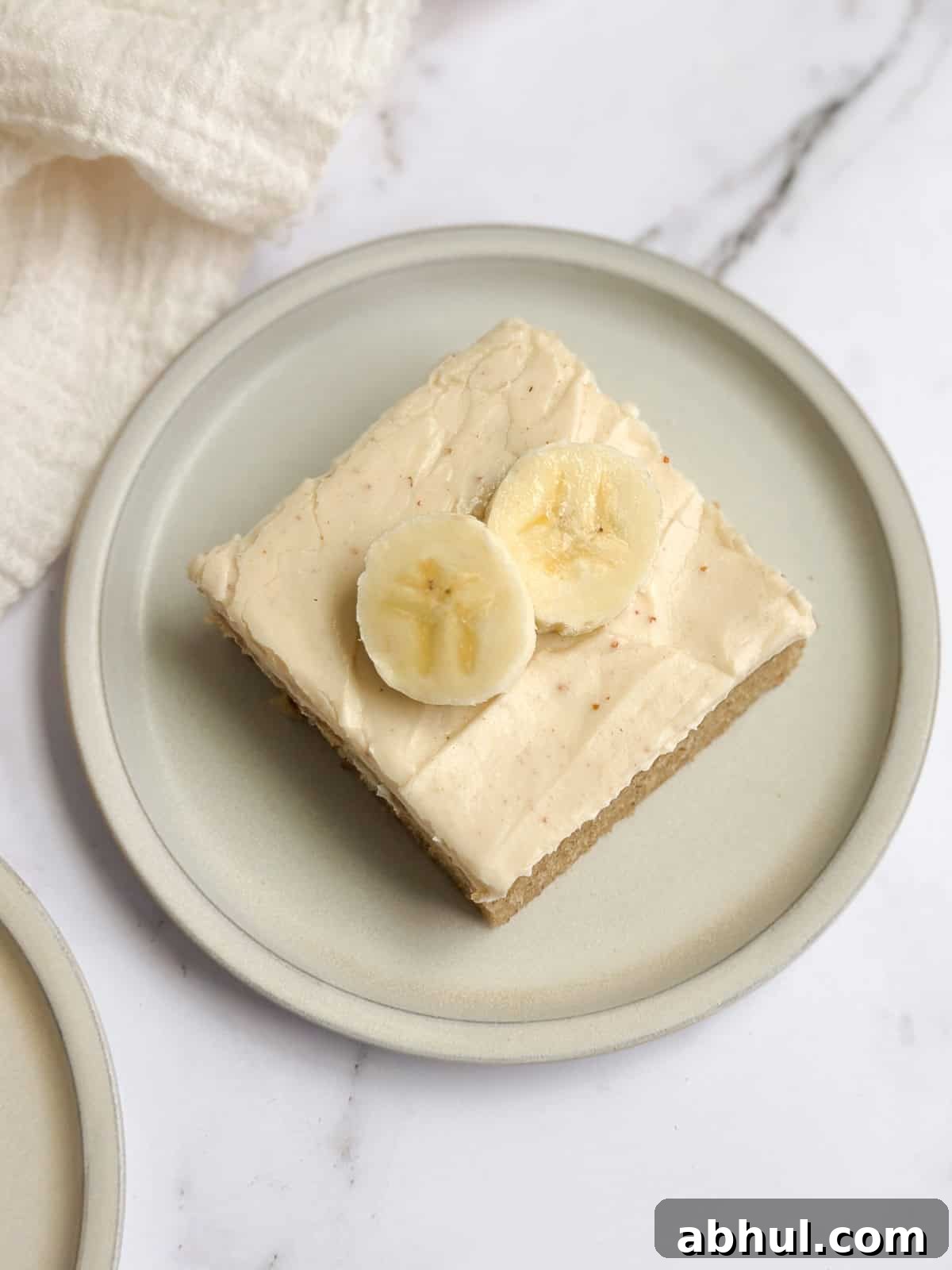 a single piece of brown butter banana sheet cake on a plate topped with fresh banana slices.