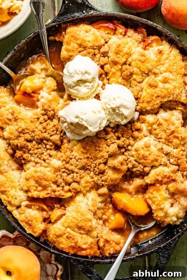 peach cobbler in a cast iron skillet topped with ice cream and fresh peaches on the side.