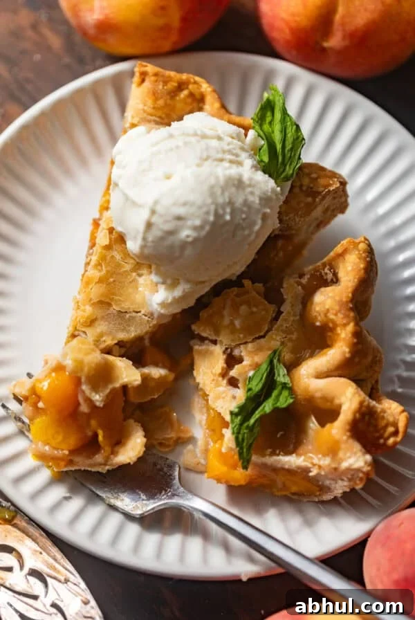 sliced peach pie on a plate topped with ice cream and mint.