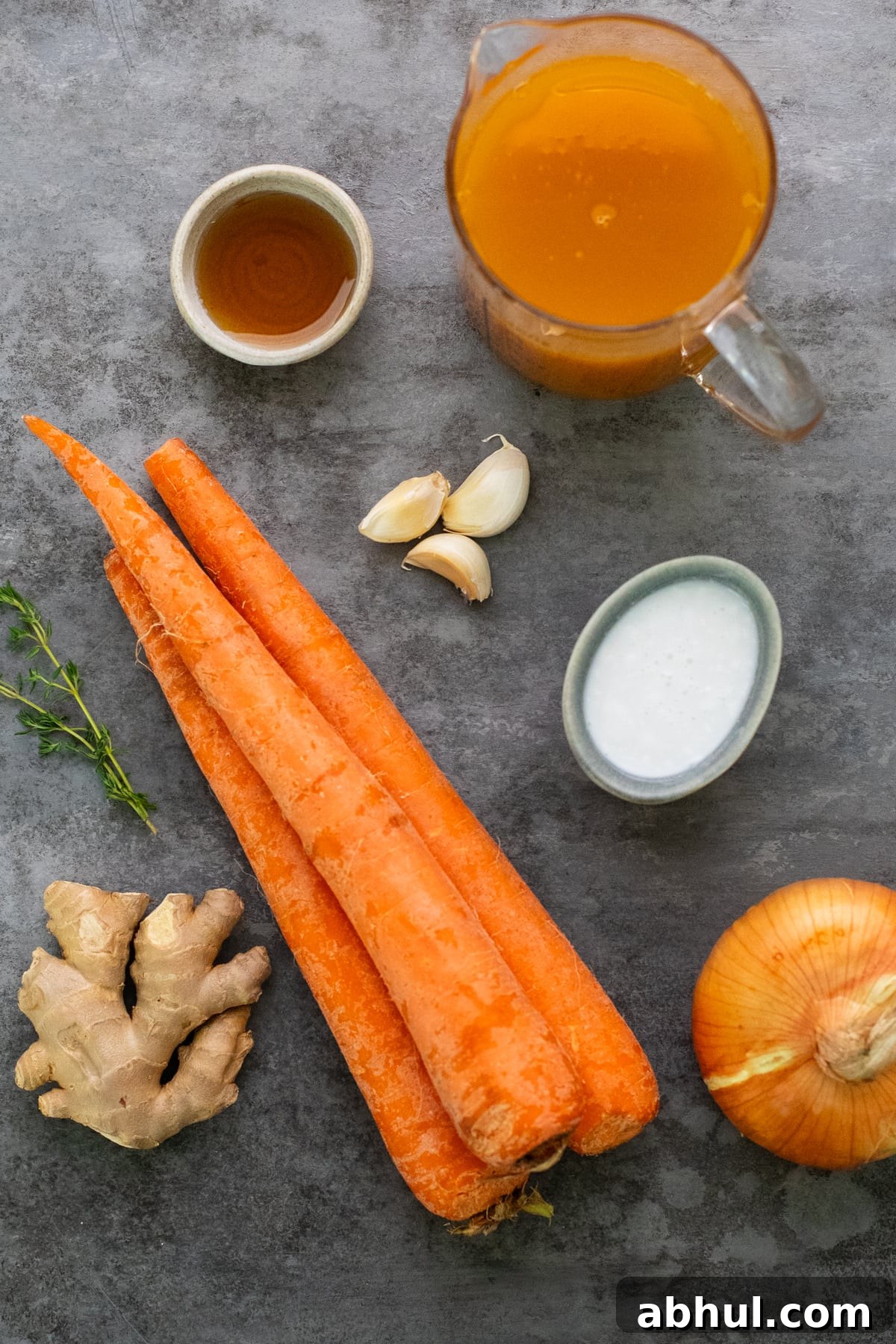 ingredients for carrot ginger soup arranged on a gray background.