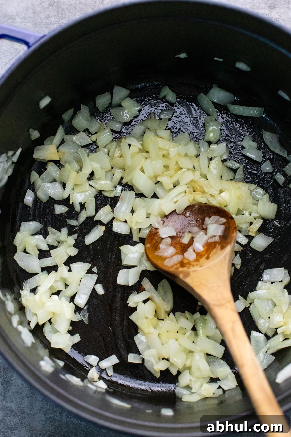 Diced onions being sautéed in a cast iron pot with wooden spoon. 