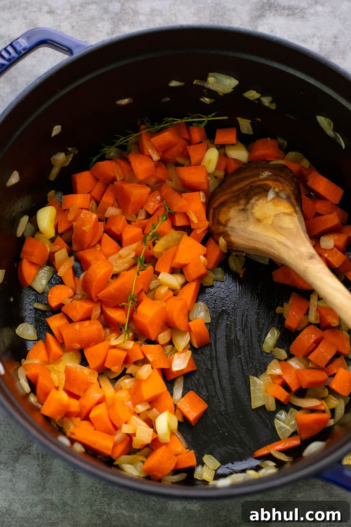 Diced carrots being sautéed in a cast iron pot with wooden spoon.