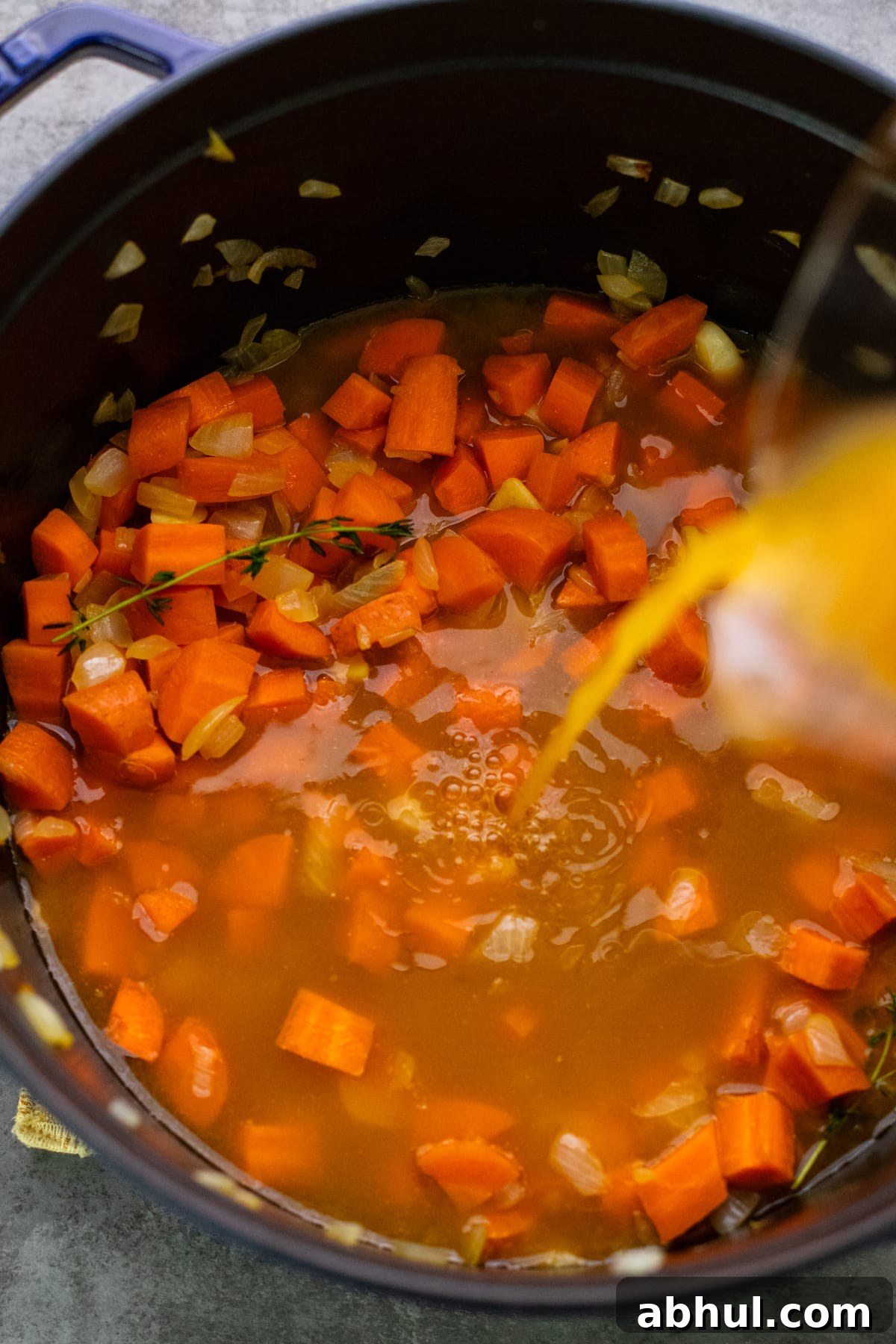 broth being poured into cast iron pot with chopped carrots.