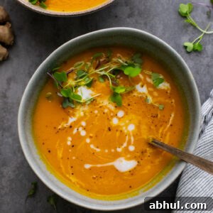 gray bowl with orange carrot soup and microgreens in it on gray background.