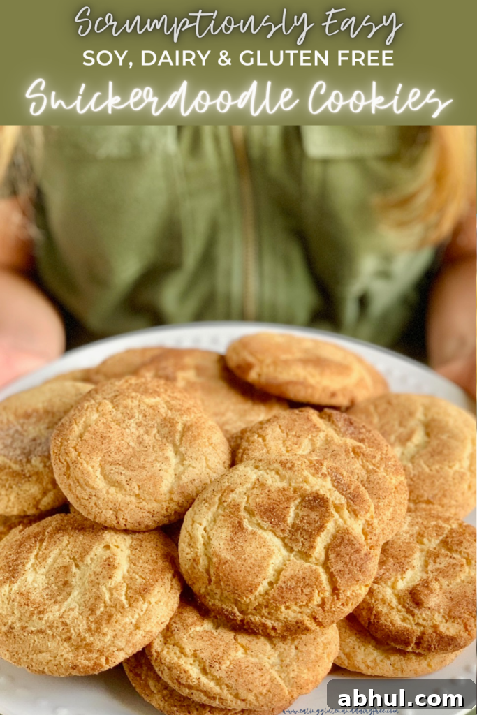 A person with a green jumpsuit holding a white plate of round baked cookies with a crackly cinnamon and sugar topping.