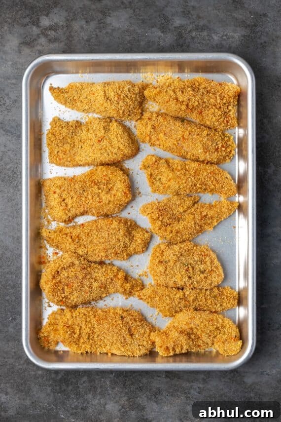 Overhead view of chicken cutlets breaded with chicken stuffing on a baking sheet.