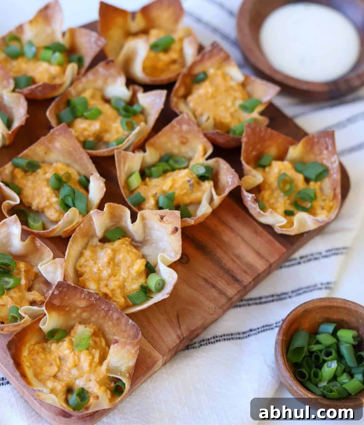 Wonton cups filled with buffalo chicken and green onion on platter.