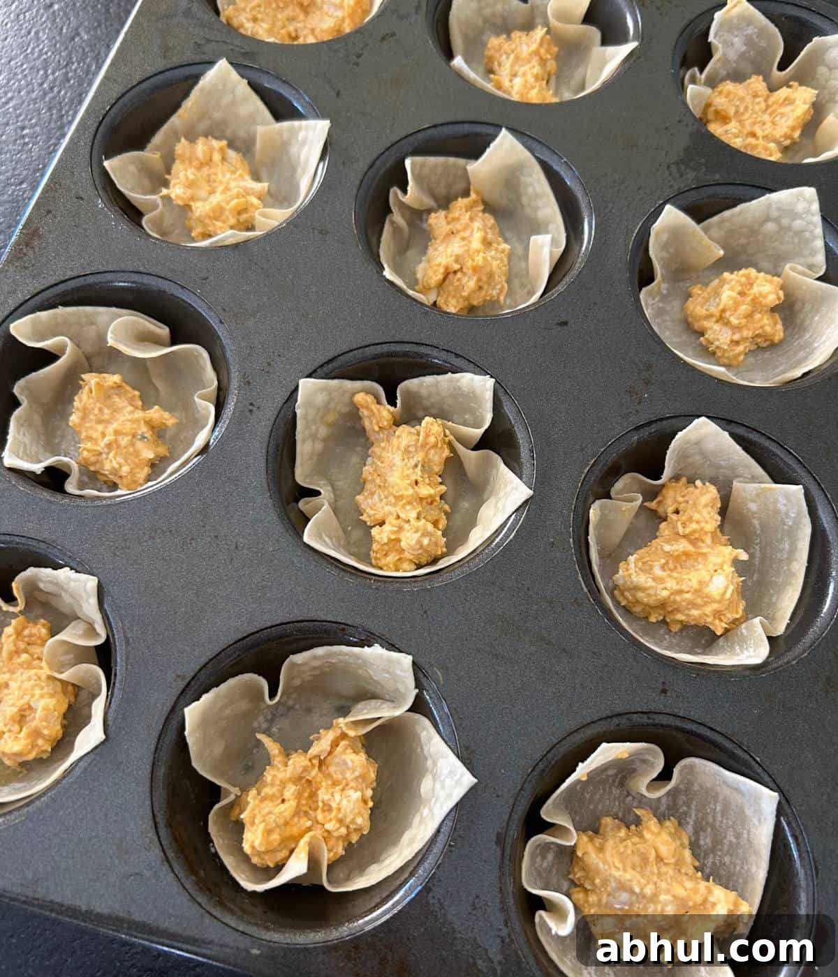 Wonton cups filled with chicken filling in muffin tin.