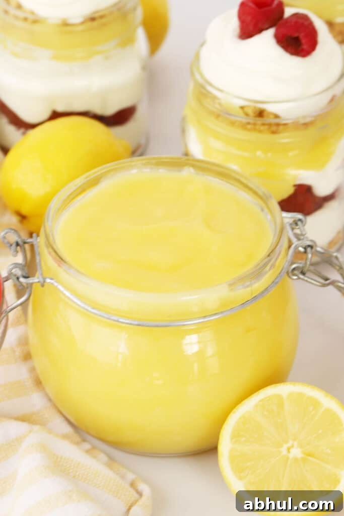 Lemon curd in a jar with lemon and raspberry parfaits in the background.