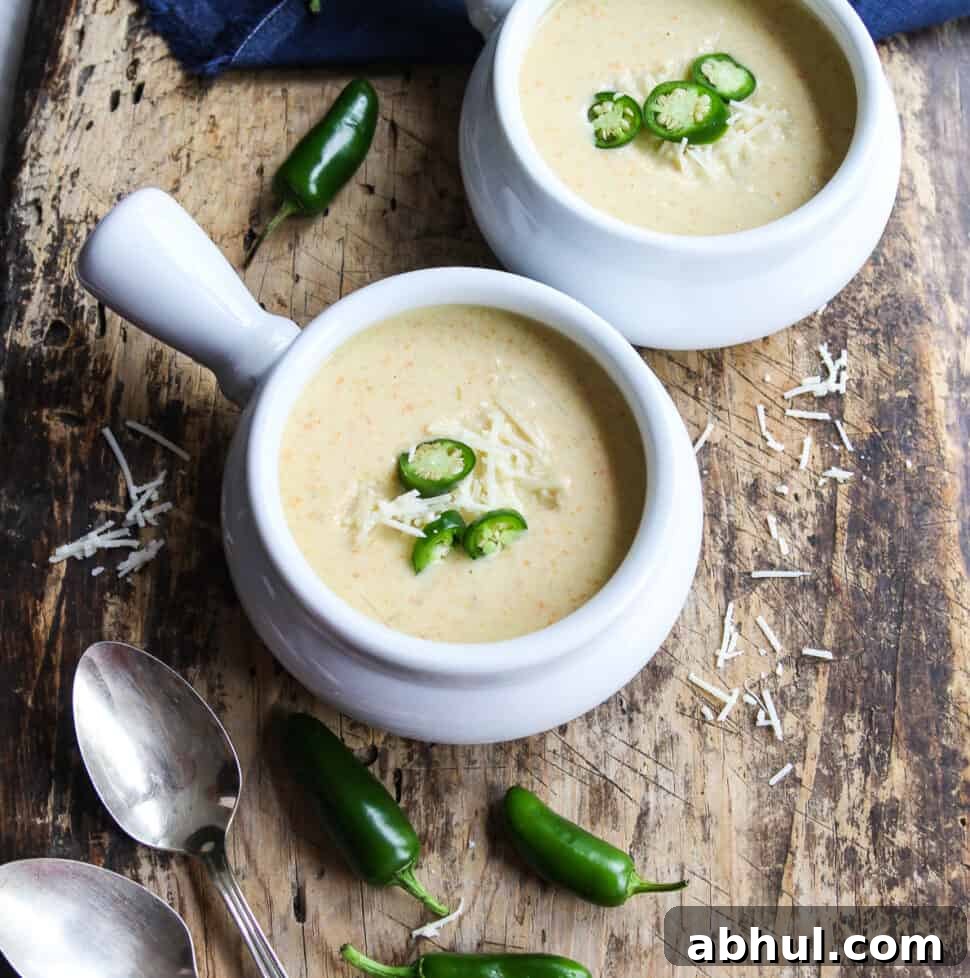 Two bowls of creamy jalapeno popper soup garnished with sliced jalapenos and cheese.