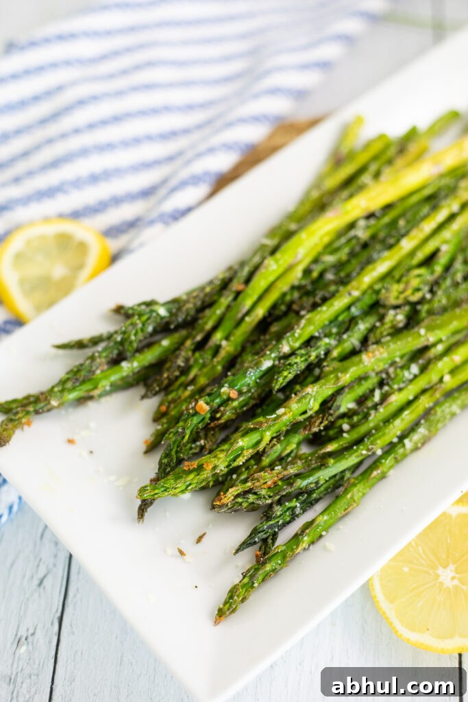 Oven roasted asparagus on a white rectangular plate next to lemon slices