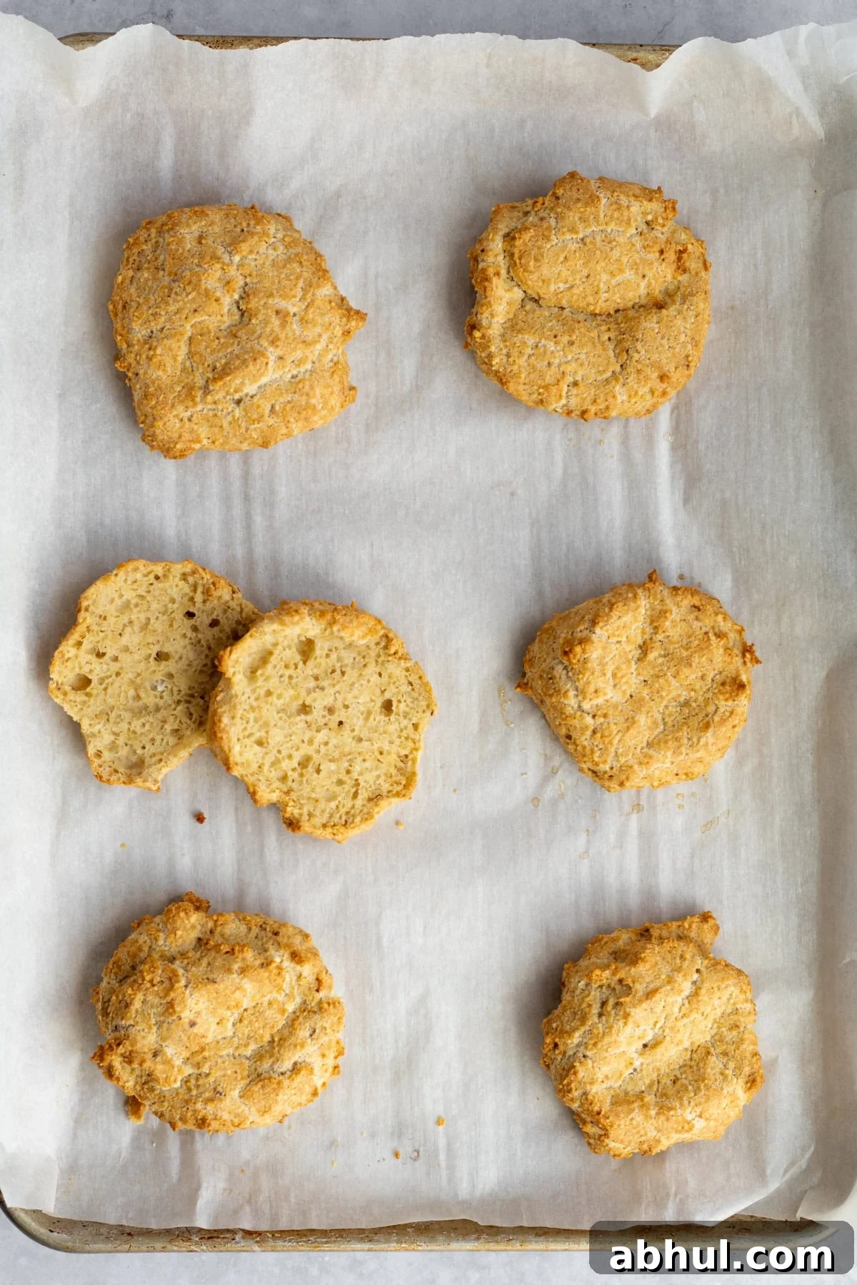 Fluffy Passover Matzo Meal Sandwich Rolls 2 matzo meal rolls on a parchment lined sheet tray with one cut open.