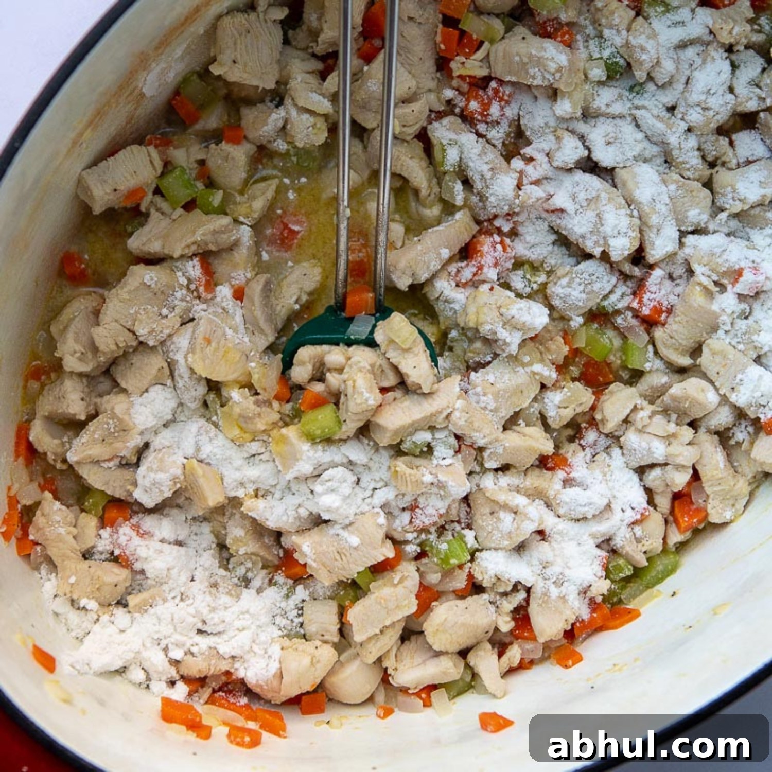 flour being stirred into the pot with cooked chicken and vegetables.