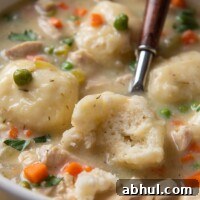 a spoon going into a bowl of chicken soup with one of the dumplings cut open
