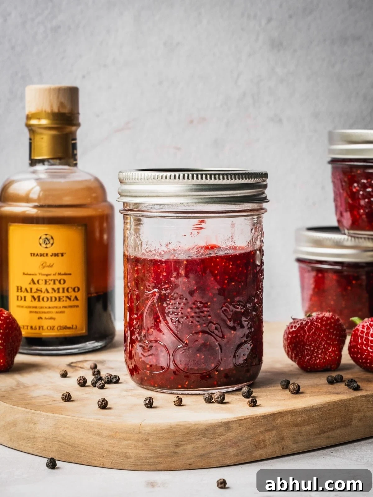 Strawberry-Balsamic Jam with Black Pepper — Homemade Recipe 2 Strawberry Balsamic Black Pepper Jam in mason jars on a wooden board with fresh strawberries, black peppercorns and a bottle of balsamic vinegar on the side.