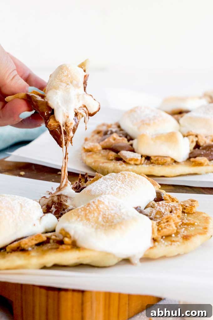 This photo shows someone pulling a piece of ooey gooey melted chocolate and marshmallow s'mores flatbread  