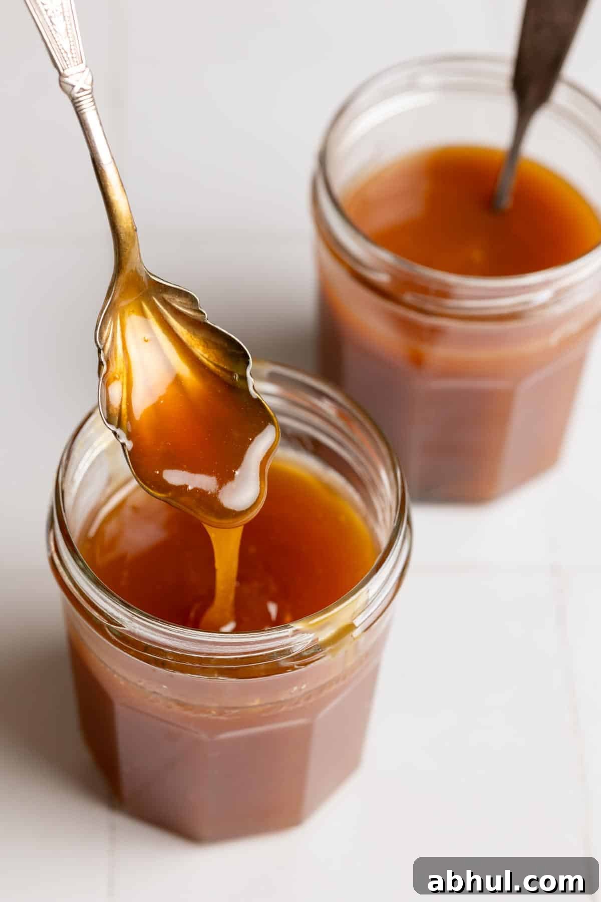 Coconut milk caramel sauce falling off a spoon into a glass jar.