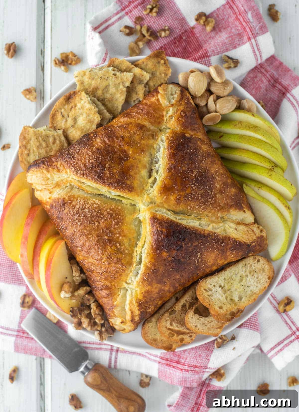 Puff pastry baked brie on plate with fruit, crackers and bread.