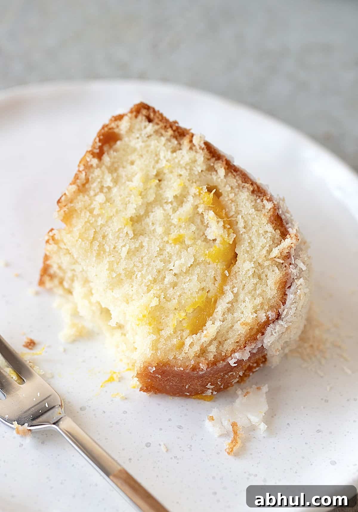 Caramelized Mango Tropical Bundt Cake Bitten slice of mango coconut cake on a white plate. A fork.