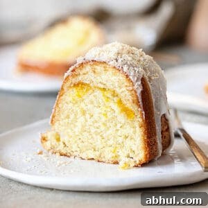 Close up slice of glazed mango coconut bundt cake on a white plate. Grey surface.