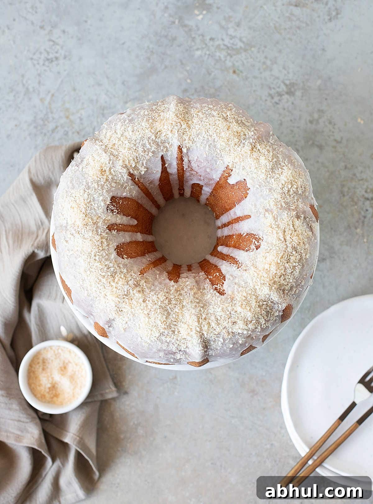 Caramelized Mango Tropical Bundt Cake Top view of glazed coconut mango bundt cake. Grey surface, cloth, stack of plates.