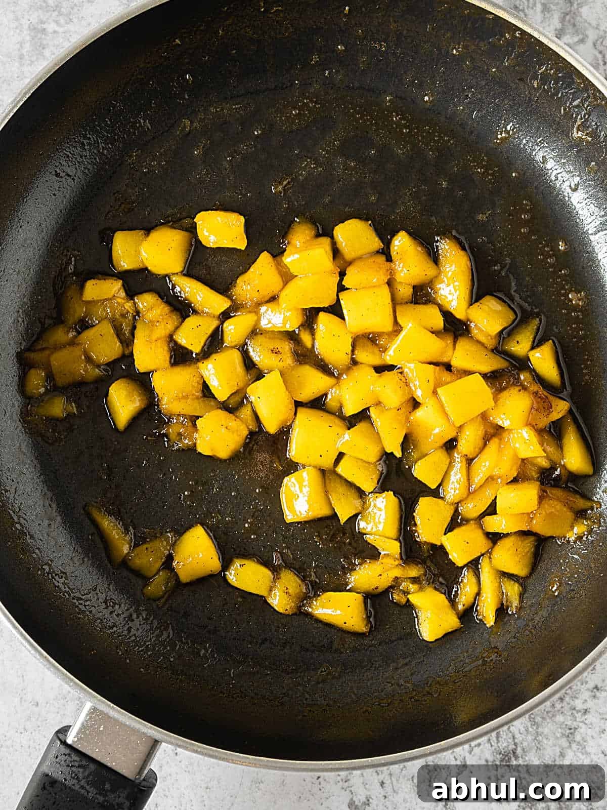 Moist Mango Coconut Bundt Cake Recipe for Tropical Desserts 4 Diced mango cooked in a black skillet.