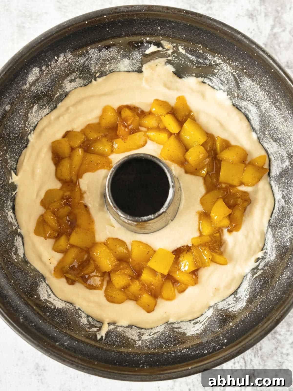 Moist Mango Coconut Bundt Cake Recipe for Tropical Desserts 5 Assembling a coconut bundt cake with mango in the middle. Black cake pan. Grey surface.