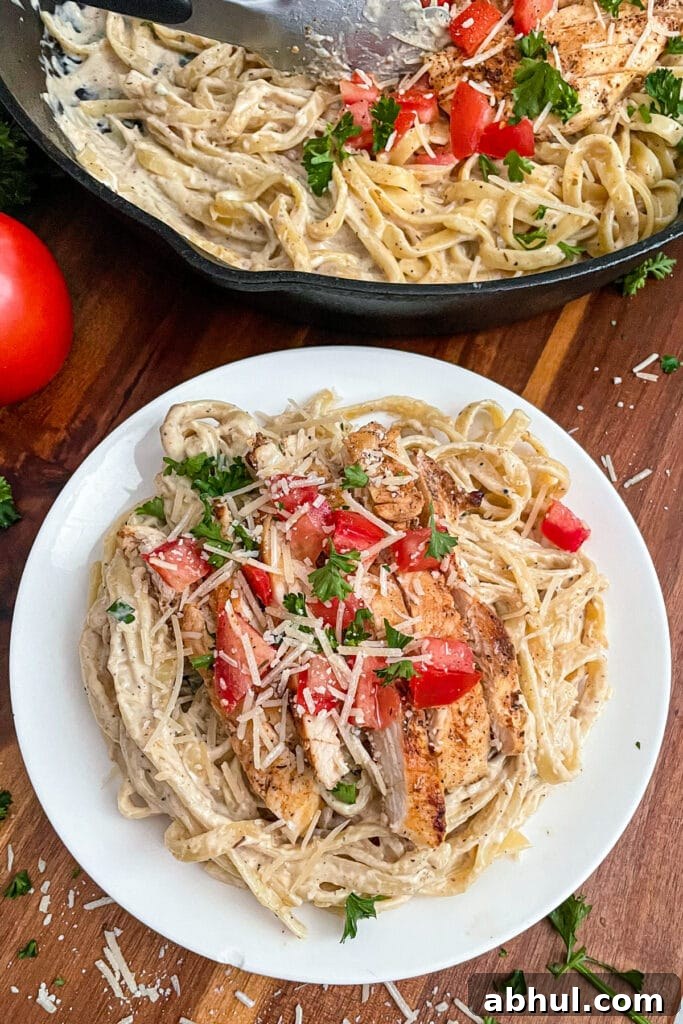 The most amazing Cajun chicken alfredo served on a white plate with a tomato on the side