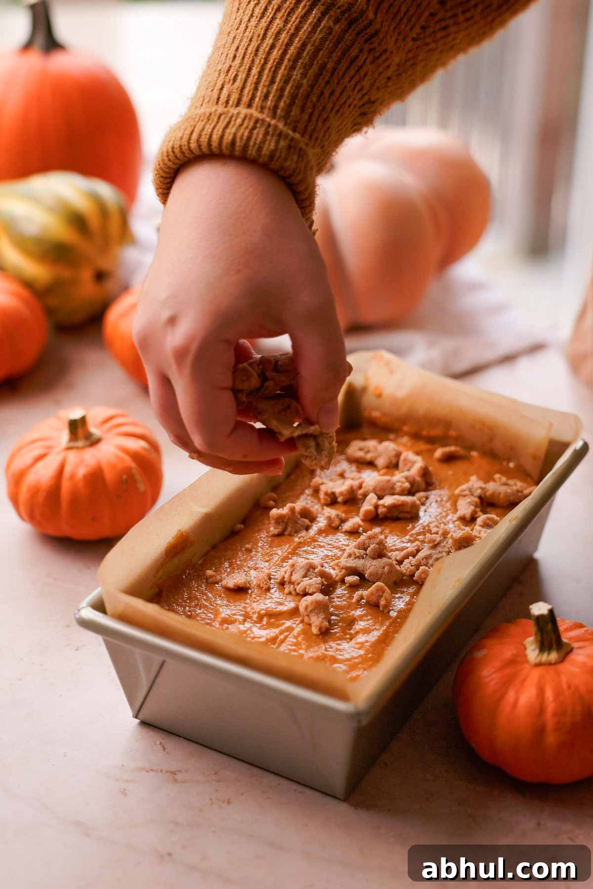 sprinkling streusel over pumpkin bread batter