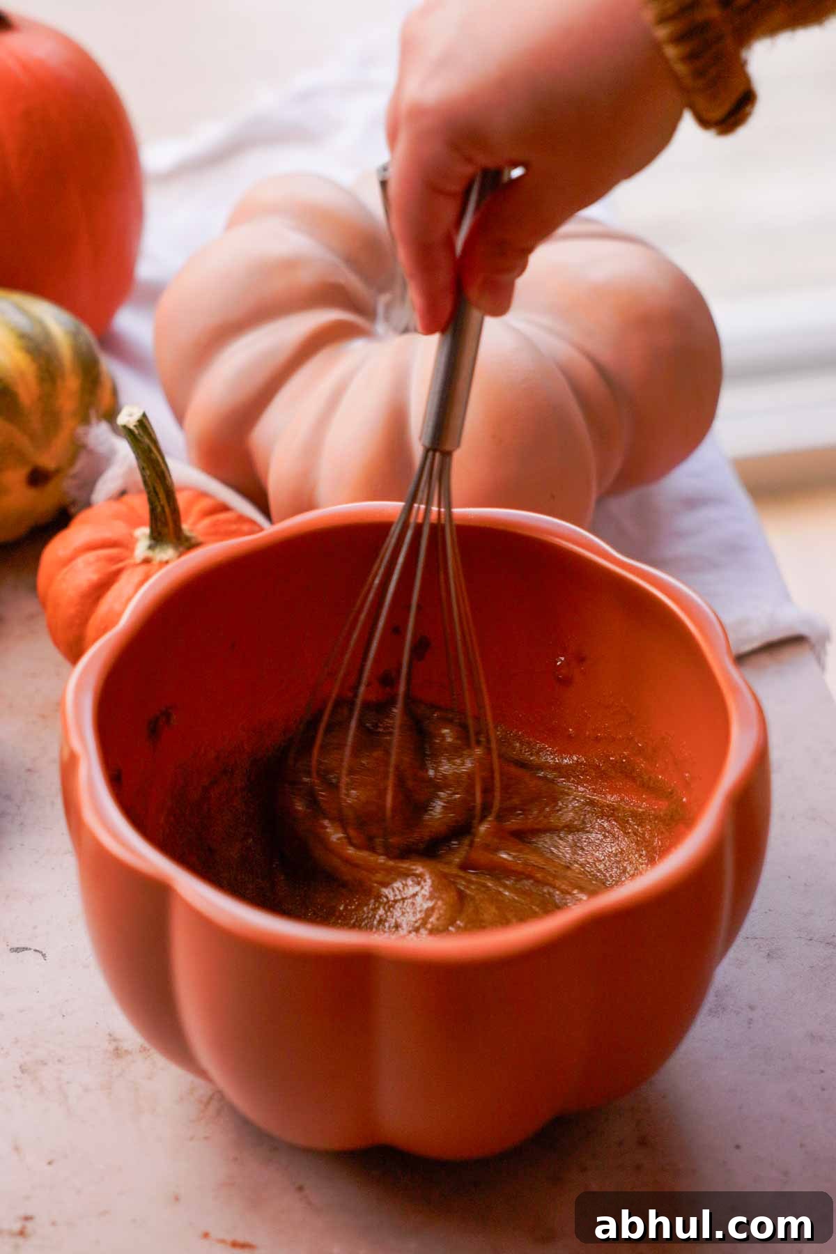 whisking eggs and brown sugar with a wire whisk in a pumpkin bowl