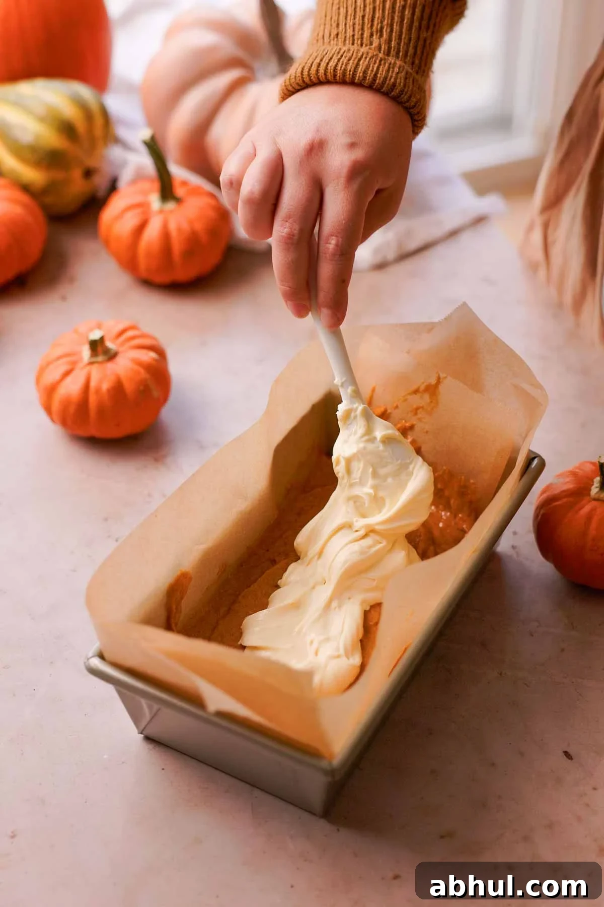 layering cream cheese batter into the center of pumpkin bread with a spoon